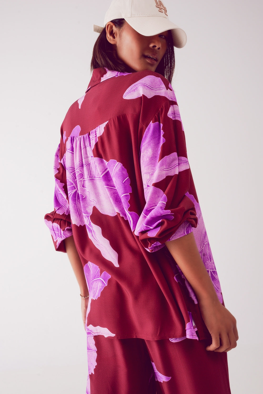 Person wearing a maroon and pink floral dress with a white cap on a plain background