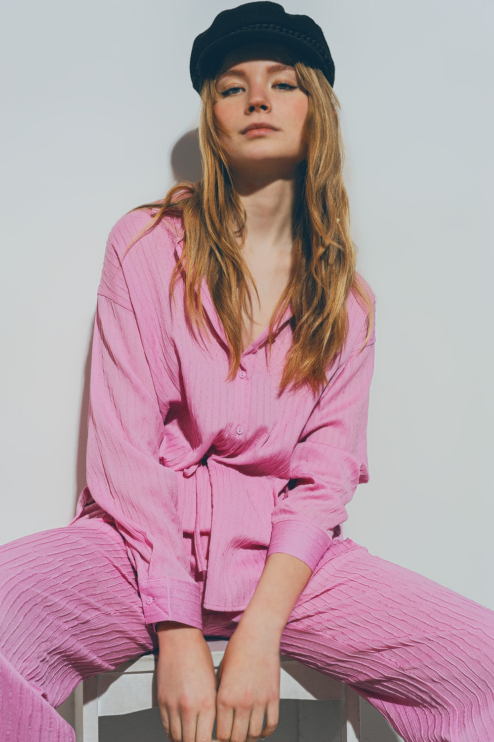 Woman wearing a pink outfit and black cap sitting on a white chair against a light gray background