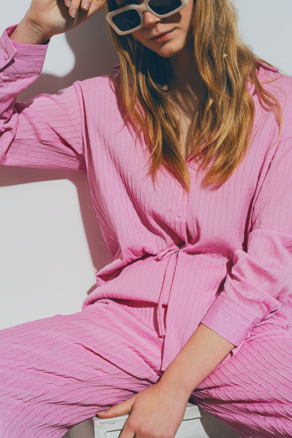 Person wearing a pink outfit with sunglasses on a light background